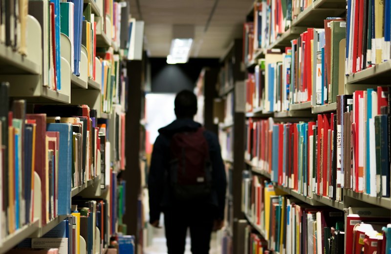 Student walking between library bookshelves